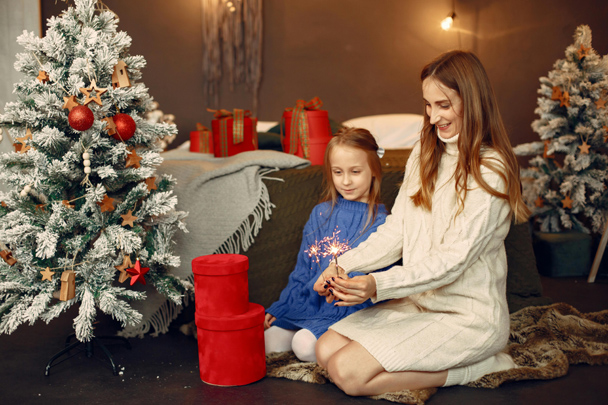 Mother and daughter opening Christmas gifts together beside a decorated tree.