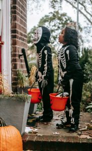 Two kids in Halloween costumes holding candy buckets while trick-or-treating