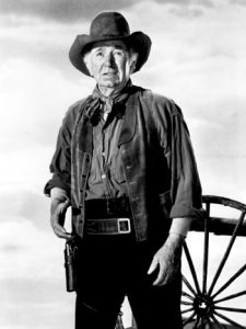 Walter Brennan in cowboy hat, vest, and gun holster from a classic western film