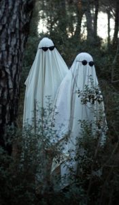 Two children in white sheet ghost costumes standing in a forest