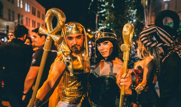 Couple in Egyptian costumes surrounded by a packed crowd in Halloween attire