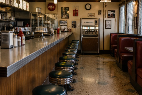 Mid-century American diner counter with a cigarette vending machine visible at the far end, part of vintage vending machines history