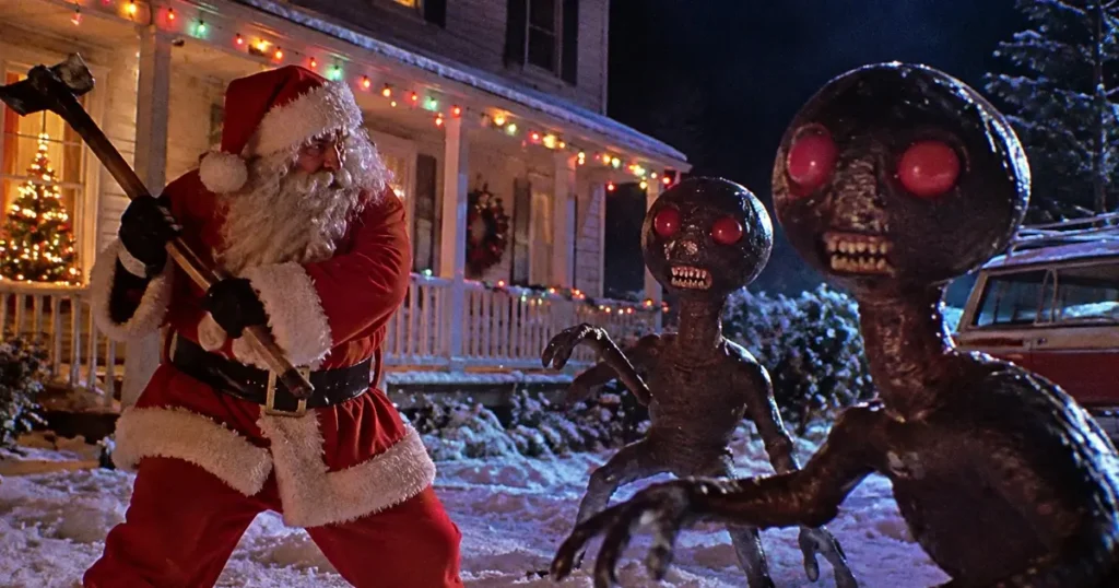 Feeders 2: Slay Bells Review hero showing Santa Claus battling two red-eyed aliens outside a snow-covered house decorated for Christmas.