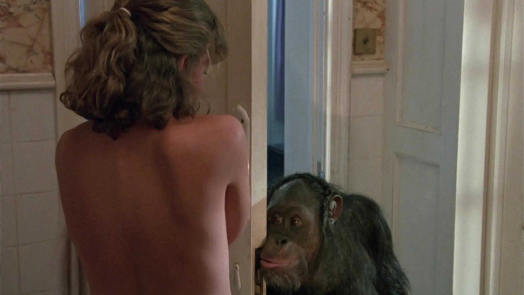 Link Review featuring Elisabeth Shue's bare back as a curious chimpanzee peeks through the bathroom doorway in the 1986 horror film.