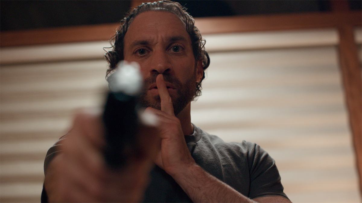 Malicious 2023 Review featuring Kevin Interdonato pointing a gun in a tense scene from the horror thriller.